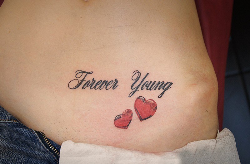Татуировки надписи. Женская тату на животе. Forever Young с сердечком.