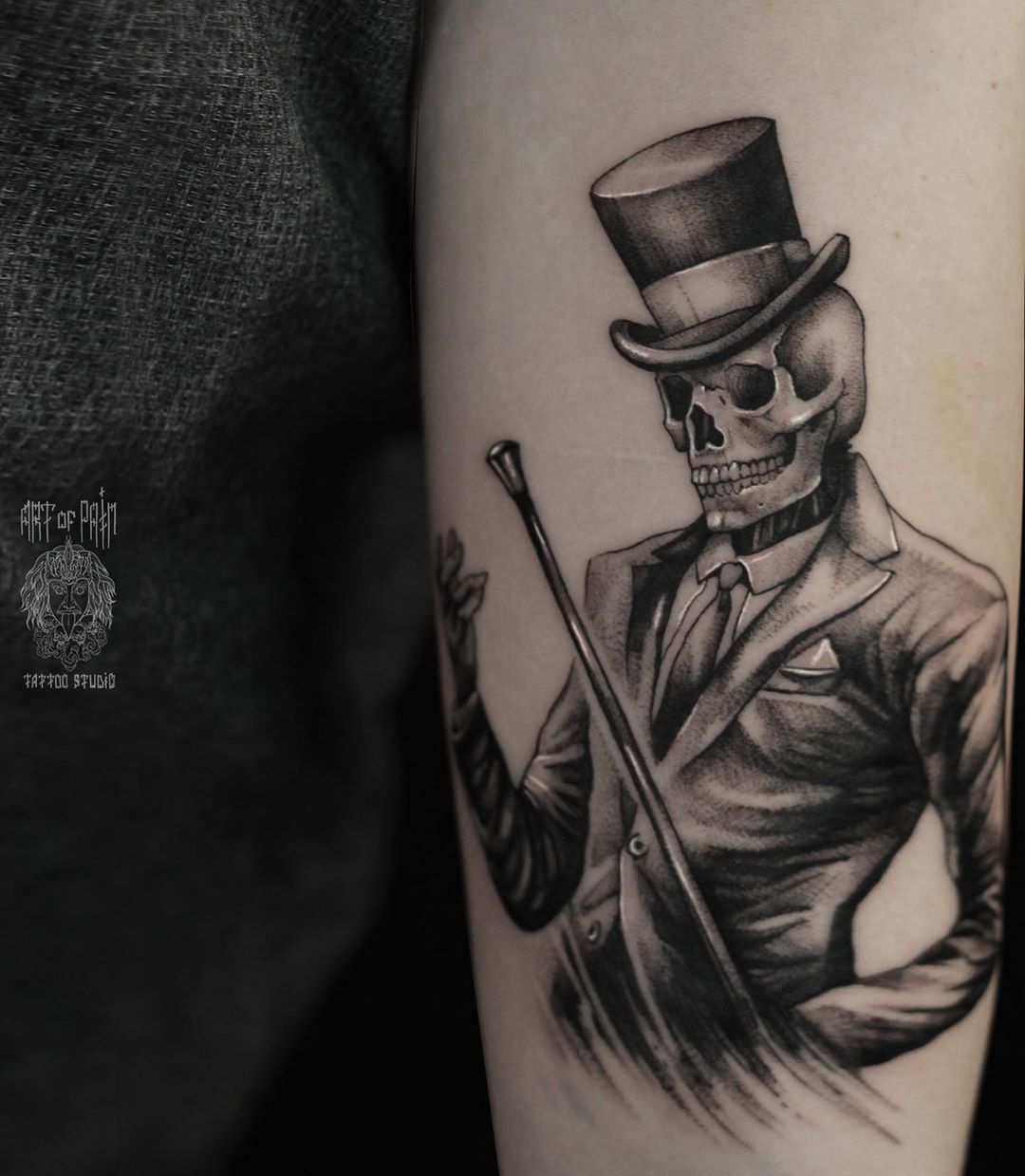 Крупным планом портрет бородатого мужчина в цилиндре с татуировкой на груди на темном фоне.