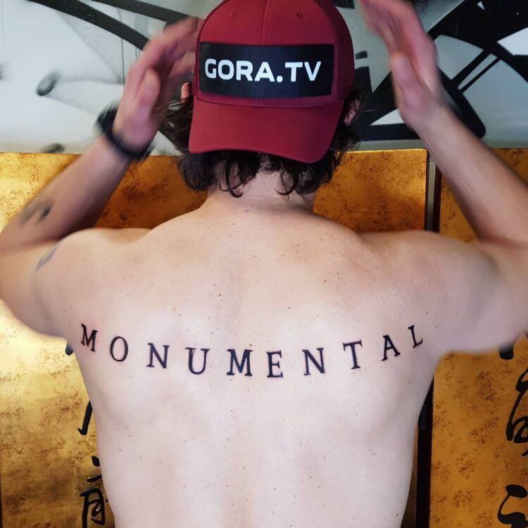 Надпись Monumental, тату на спине у парня