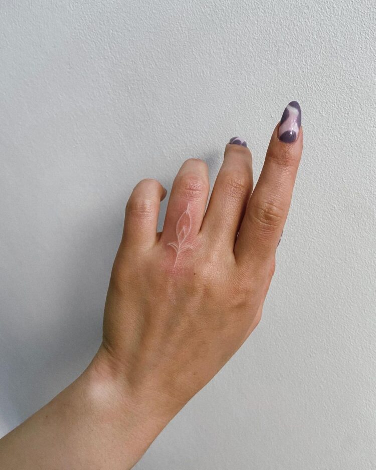 Белая татуировка на пальце у девушки